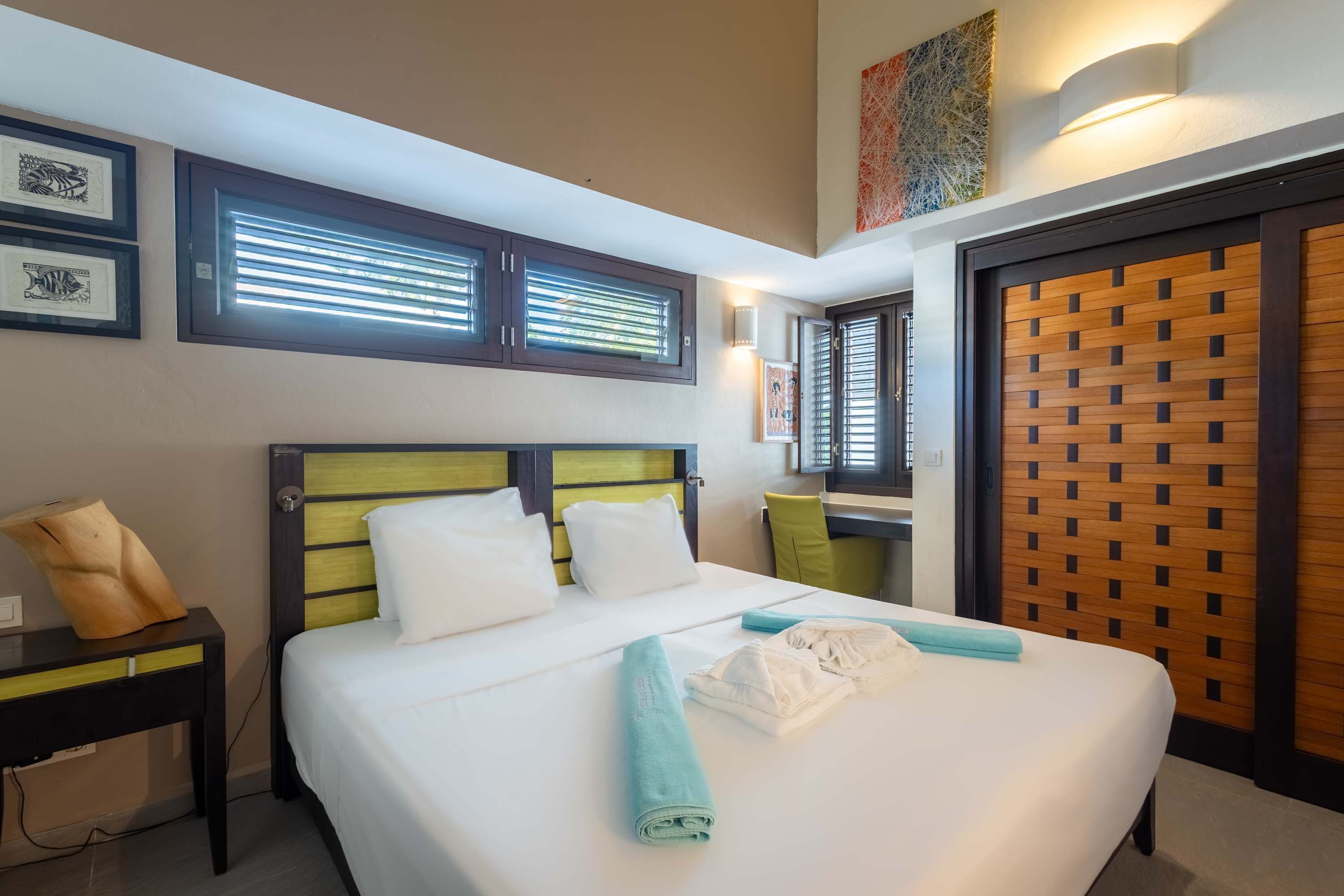 A hotel room with a bed, a nightstand, a chair, a window with blinds, and a door with a wooden panel.