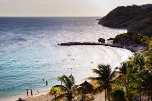 Una playa con agua azul cristalina, palmeras y un acantilado rocoso.