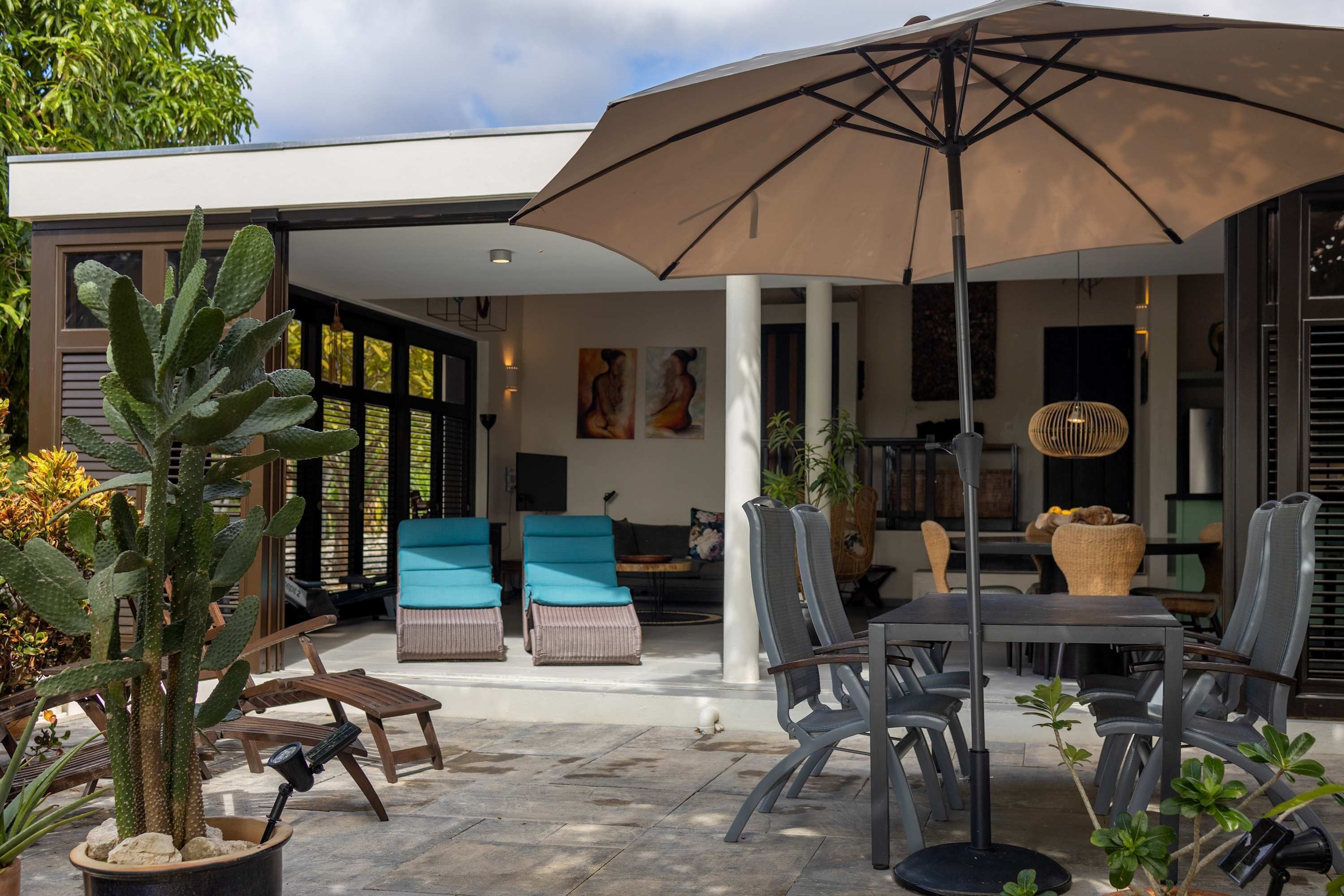 En udendørs patio med et bord, stole, en stor parasol og forskellige planter.