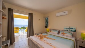 A hotel room with a bed, a nightstand, a window with curtains, a view of the sea, and a balcony with chairs. - Tropical Twilight Haven Unwind in Style (Sint Willibrordus)