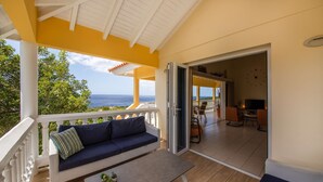 A balcony with a sofa and table, a view of the ocean, and an open door leading to a dining area. - Tropical Twilight Haven Unwind in Style (Sint Willibrordus)