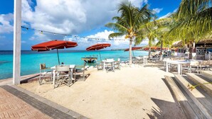 A beachside restaurant with outdoor seating, palm trees, and a view of the ocean. - Tropical Twilight Haven Unwind in Style (Sint Willibrordus)