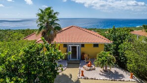 A yellow building with a red-tiled roof, surrounded by greenery and a view of the ocean. - Tropical Twilight Haven Unwind in Style (Sint Willibrordus)