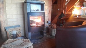 Interior acogedor de una cabaña con estufa de leña, un sofá y una cesta de leña.