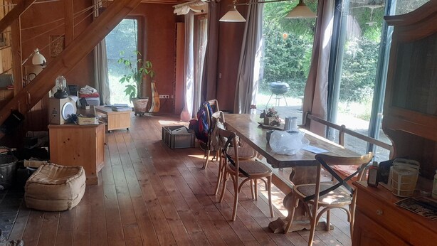 Un interior rústico de madera con un comedor, sillas de madera, una mesa, un ventanal grande y una chimenea.