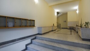Eine Treppe mit Marmorstufen führt zu einer Zwischenebene, ein Holzboden mit Glastüren und ein Empfangstisch mit Pflanzen.