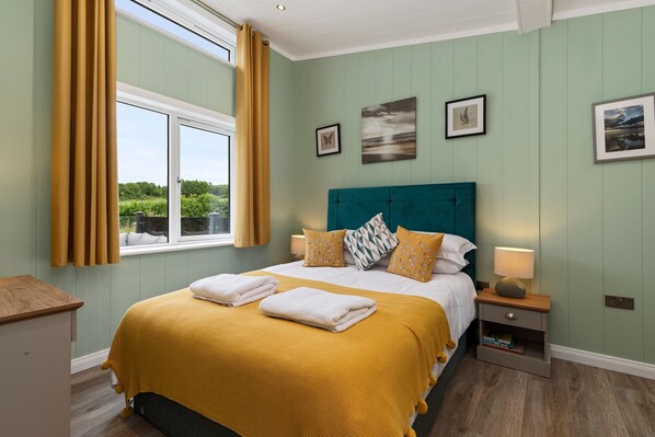 A bedroom with a bed, a nightstand, a window with curtains, and wall-mounted artwork. - Mallard s Rest - Countryside Hot Tub (Narberth)