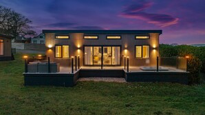 A modern house with a central entrance, large windows, and a well-lit exterior at dusk. - Mallard s Rest - Countryside Hot Tub (Narberth)