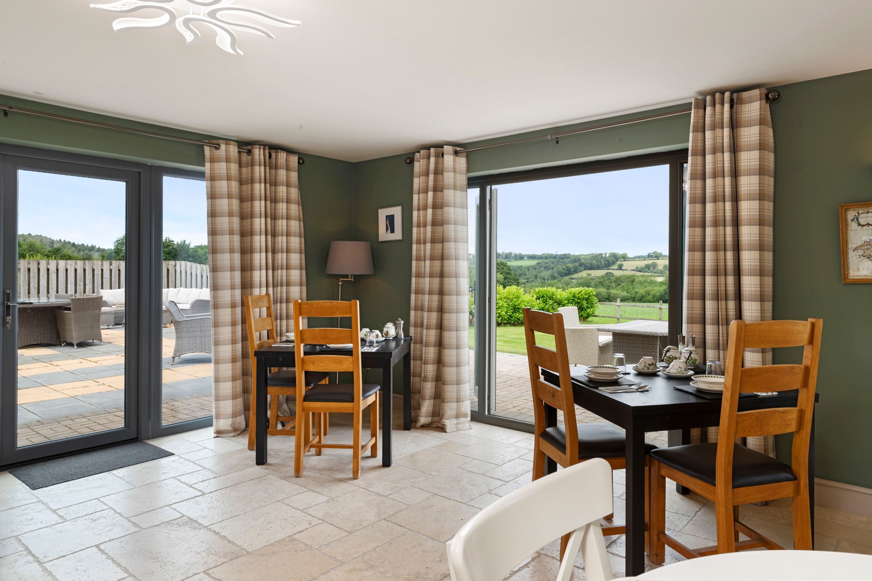A dining area with a table set for four, two wooden chairs, a lamp, and a view of the outdoors.