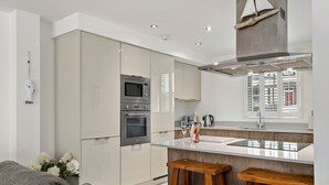 A modern kitchen with a central island, stainless steel appliances, and a window with blinds. - Maes-y-berllan - Close to Village and Beach (Saundersfoot)