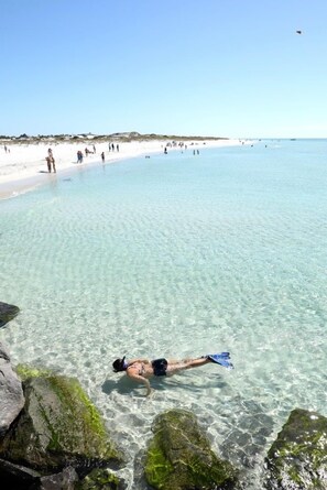 Una playa despejada con gente nadando y caminando, y una persona haciendo snorkel.