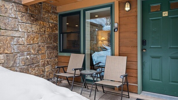 A stone exterior wall, a green door with the number 15, and two wicker chairs outside.