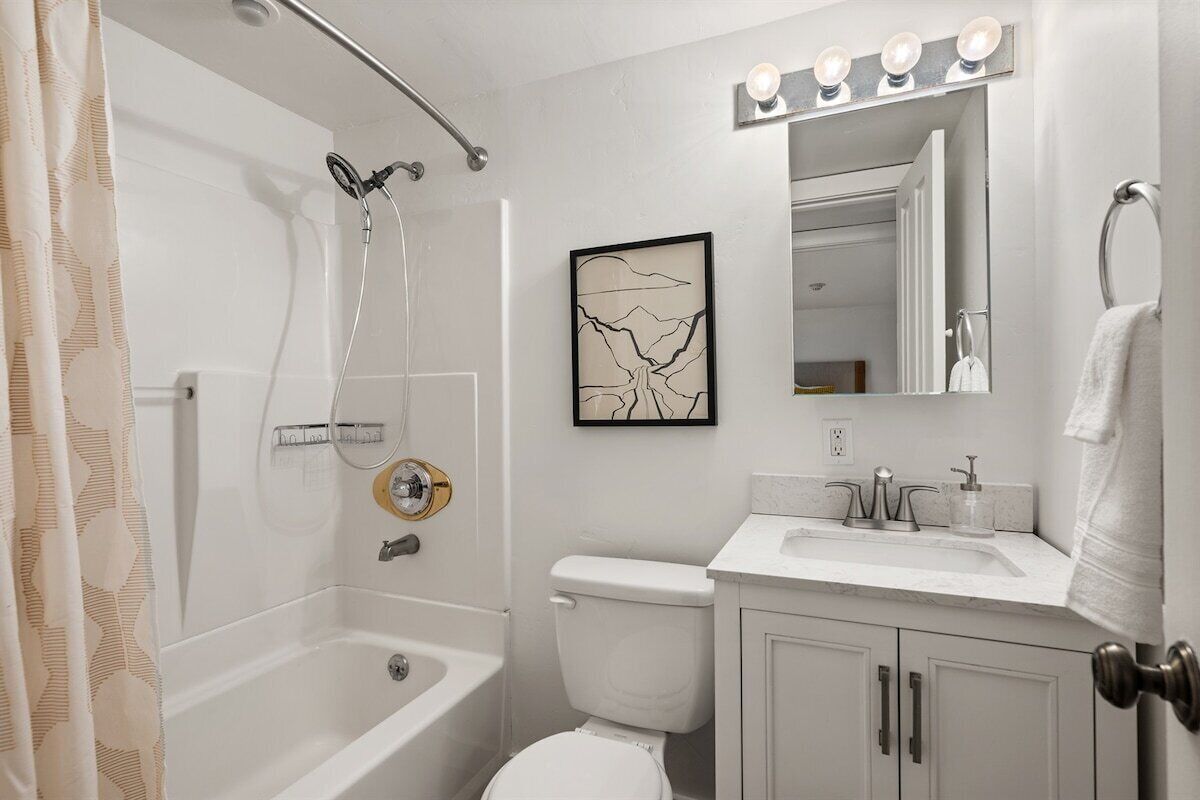 A bathroom with a bathtub, toilet, and sink. There is a showerhead, a towel rack, and a framed picture on the wall.