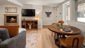 A modern living room with a fireplace, a TV, a dining area with a table and chairs, and a cozy seating area with a sofa.