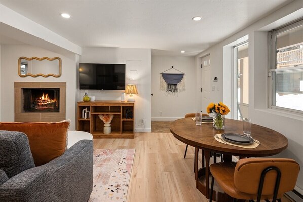 Una sala de estar moderna con chimenea, un televisor, un comedor con mesa y sillas, y una zona de estar acogedora con sofá.