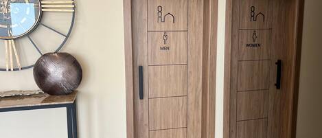 Two wooden doors with gender-specific symbols and a wall-mounted clock.