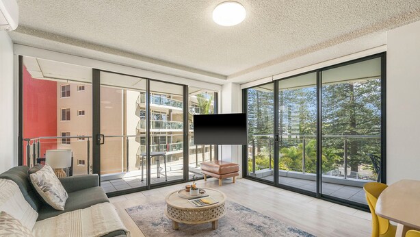 A modern living room with a sofa, round coffee table, and a TV on a balcony with large windows. - Tasman Towers 4 - Conveniently located in the CBD (Port Macquarie)