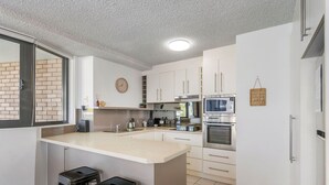 A modern kitchen with a central island, stainless steel appliances, and white cabinetry. - Tasman Towers 4 - Conveniently located in the CBD (Port Macquarie)