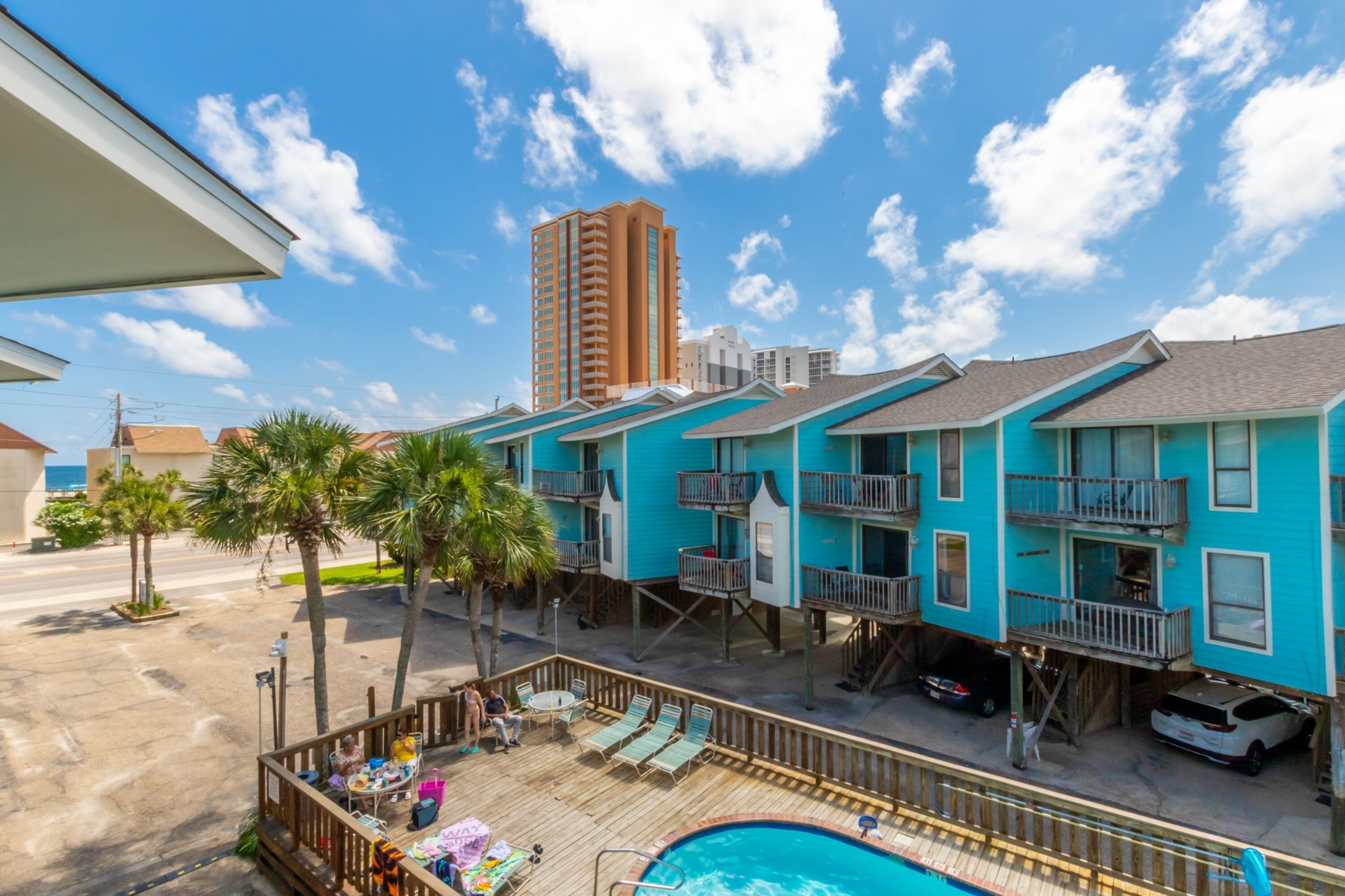 A turquoise building with balconies, a pool, and palm trees.
