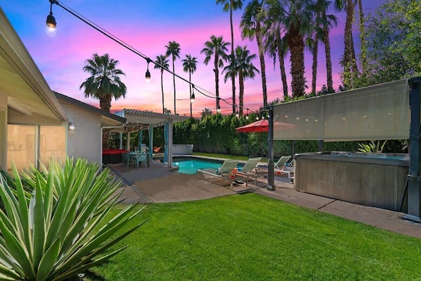Un patio trasero con piscina, palmeras y un área de patio techada.