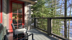 A balcony with a red door, a chair, and a view of trees and a body of water. - Bright, Mountain Modern Breckenridge Condo 1 Bedroom Condo (Breckenridge)