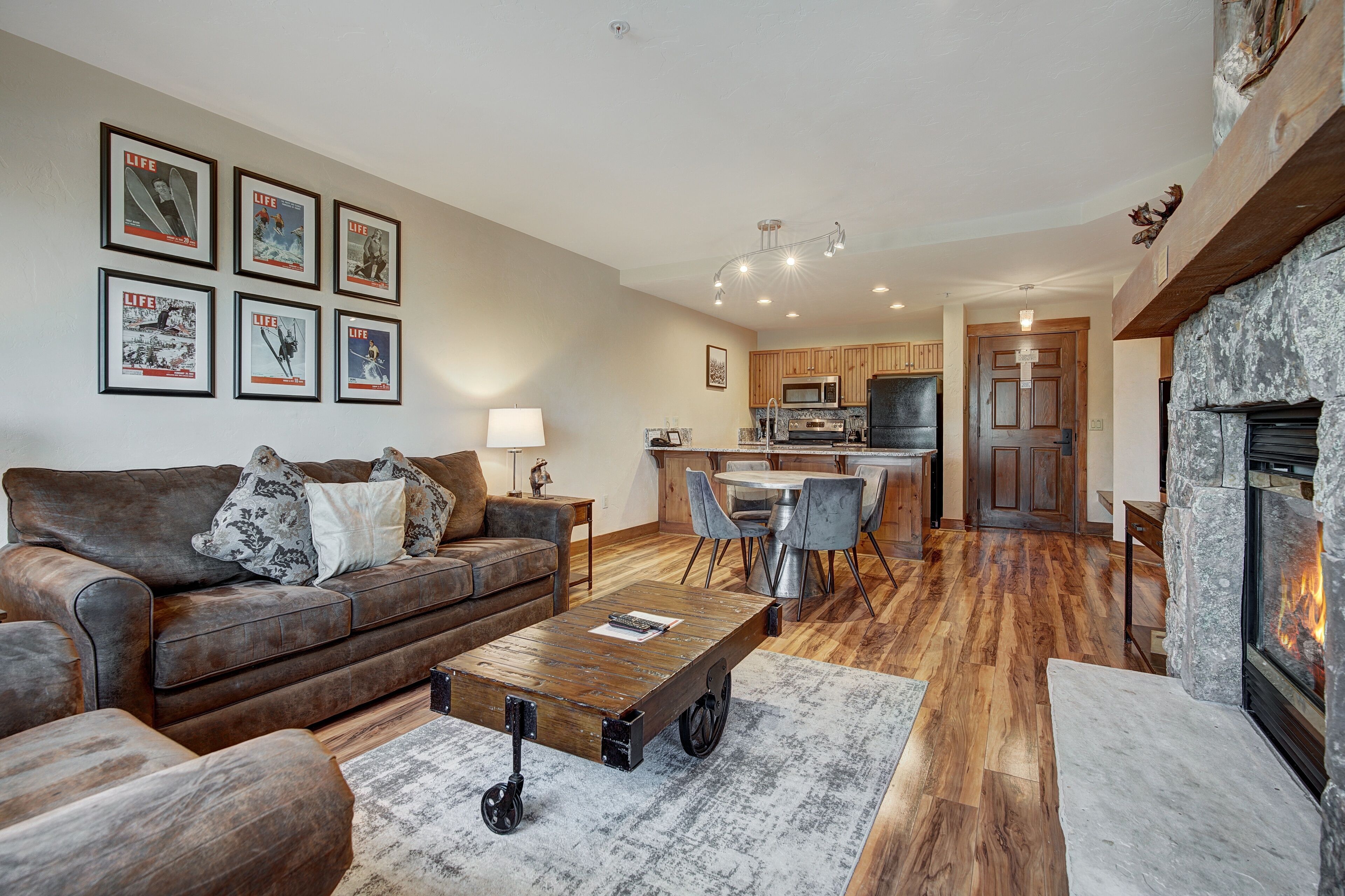 A living room with a brown leather sofa, a coffee table with wheels, a fireplace, and a kitchen in the background.