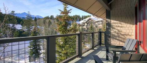 Un balcon avec vue sur une montagne enneigée, des arbres et un bâtiment en arrière-plan.