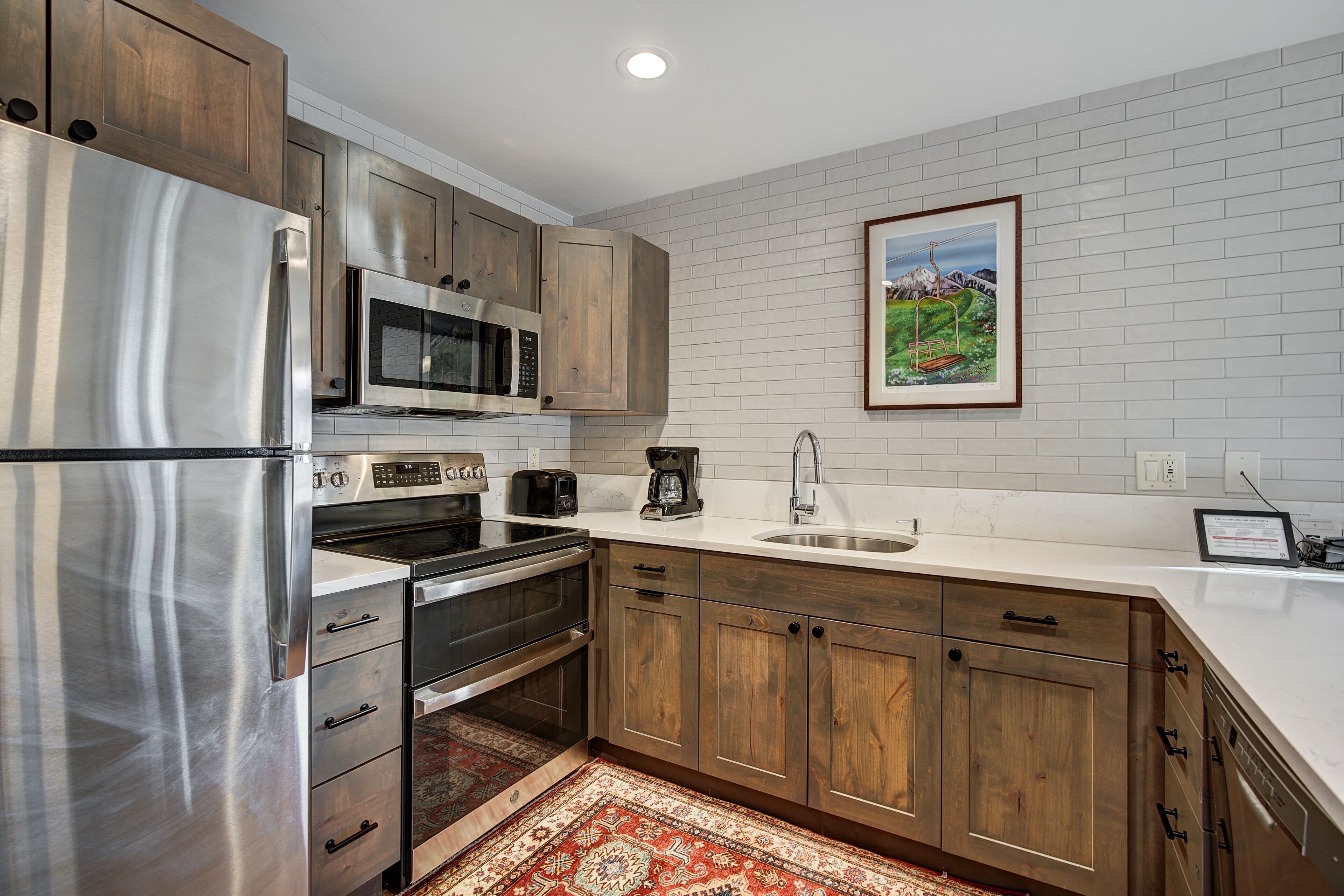 A modern kitchen with stainless steel appliances, wooden cabinets, and a white tiled backsplash.