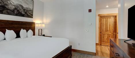 A bedroom with a large bed, wooden headboard, bedside lamps, a TV, and a wooden door.