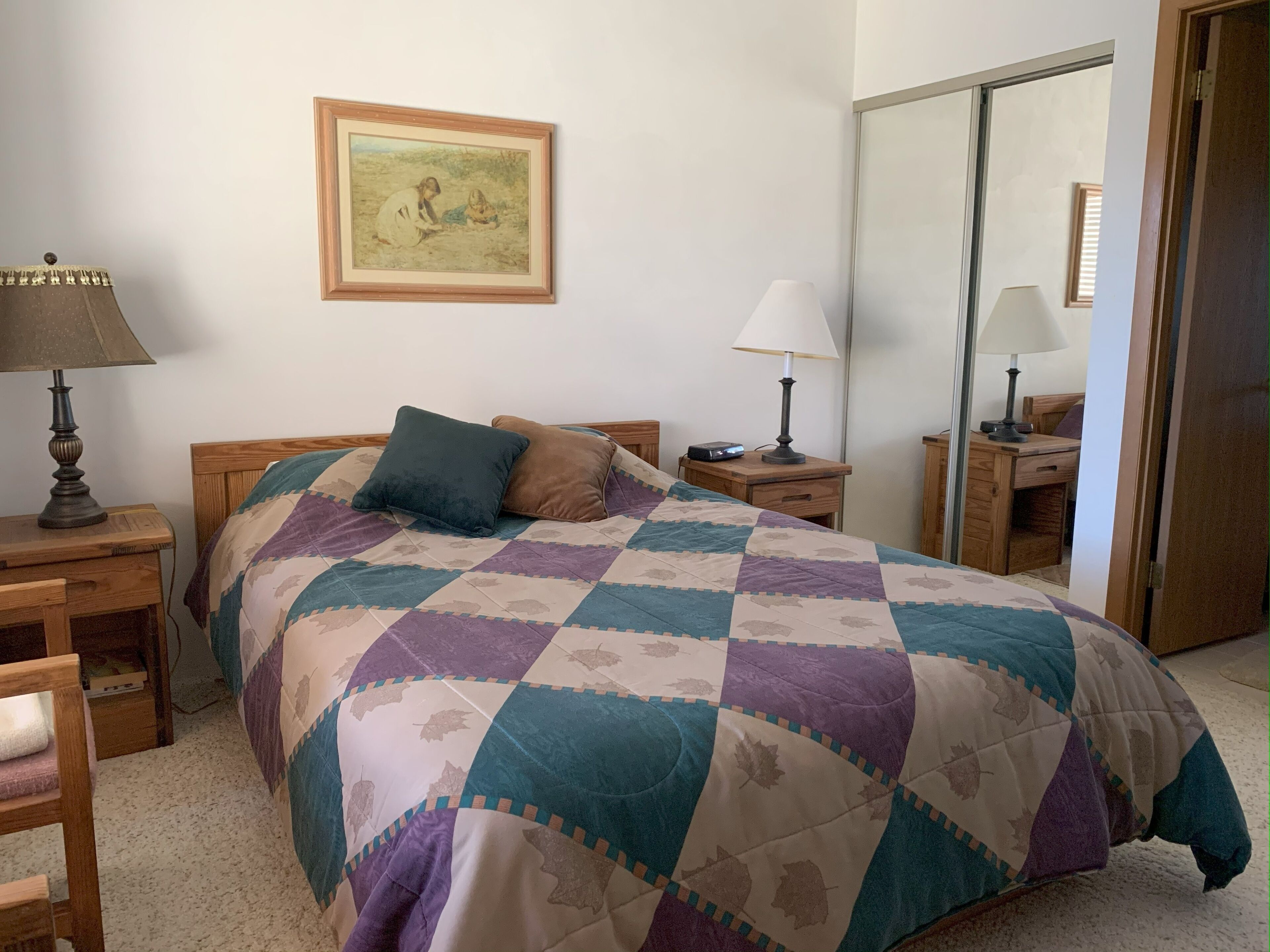 Een slaapkamer met een bed, twee nachtkastjes, een lamp, een spiegel en een ingelijst schilderij aan de muur.