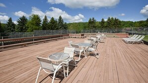 Eine Holzterrasse mit Sitzgelegenheiten im Freien, darunter Tische und Stühle, sowie ein Poolbereich mit Liegestühlen.