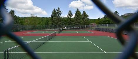 A tennis court with a net, surrounded by trees and a clear sky.