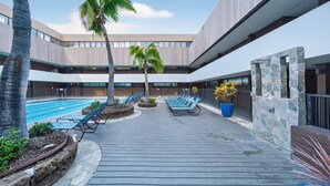 A poolside area with lounge chairs, palm trees, and a stone wall. - Chic Dt Honolulu Executive Condo 1 Bedroom Condo (Honolulu)