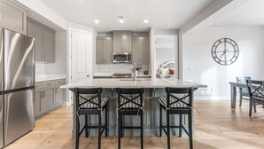 A modern kitchen with stainless steel appliances, a central island with bar stools, and a wall clock. - Desert Rose Hideaway 5 Bedroom Home (Washington)