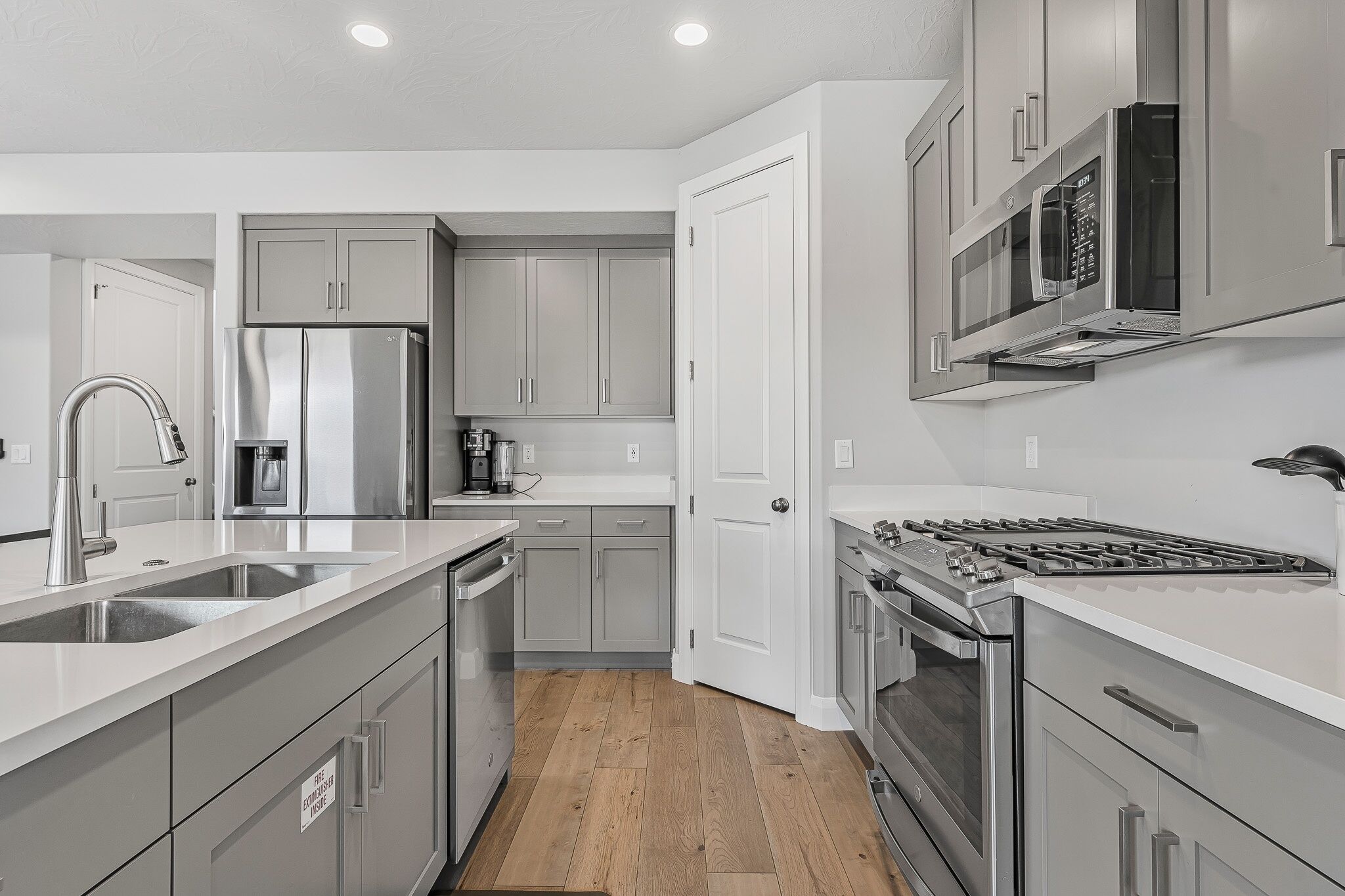 A modern kitchen with stainless steel appliances, grey cabinets, and a wooden floor.