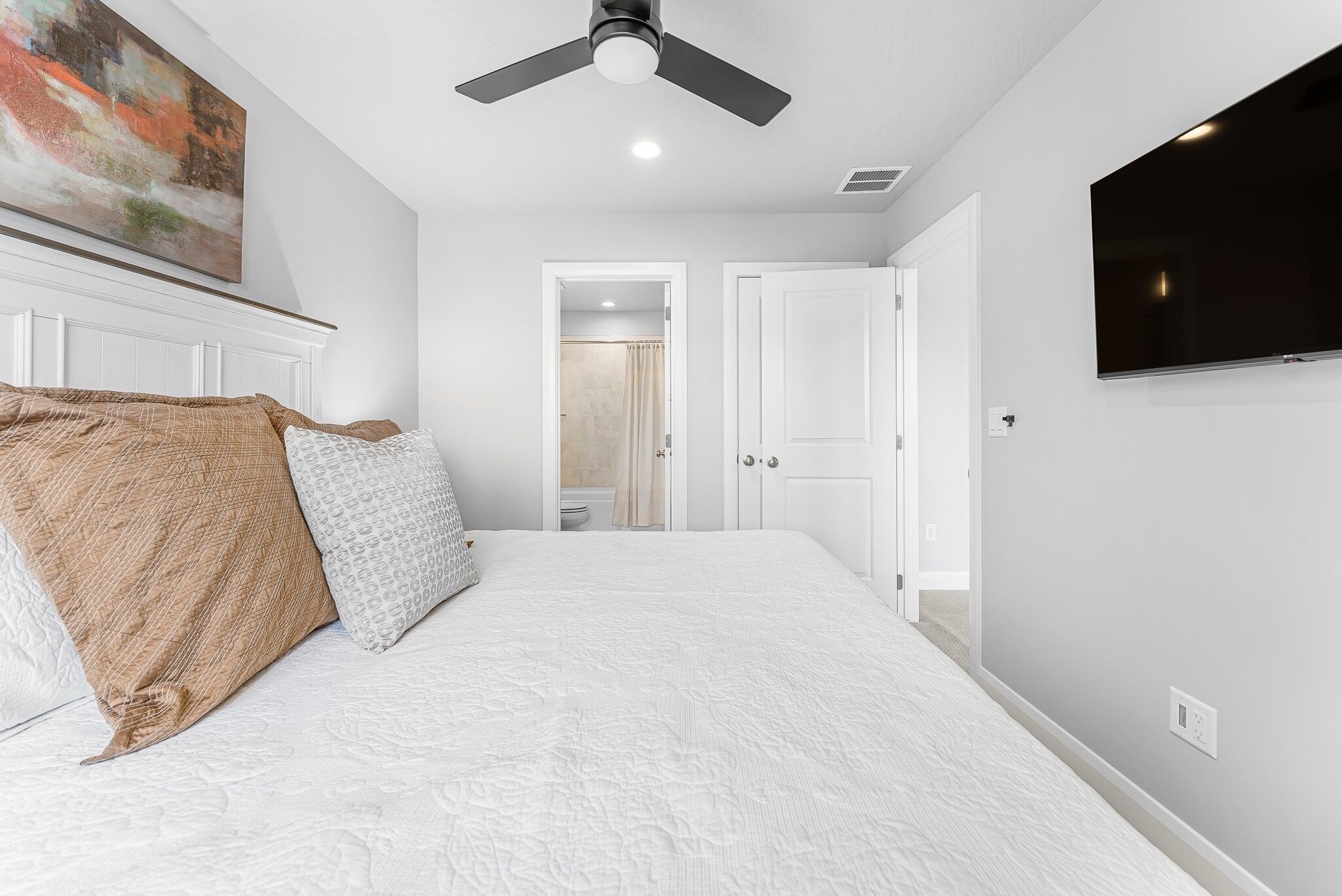 A bedroom with a bed, a ceiling fan, a TV, and a painting on the wall.