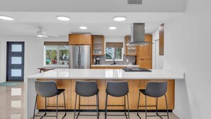 Una cocina moderna con una isla central, taburetes de bar, electrodomésticos de acero inoxidable y vistas al exterior.