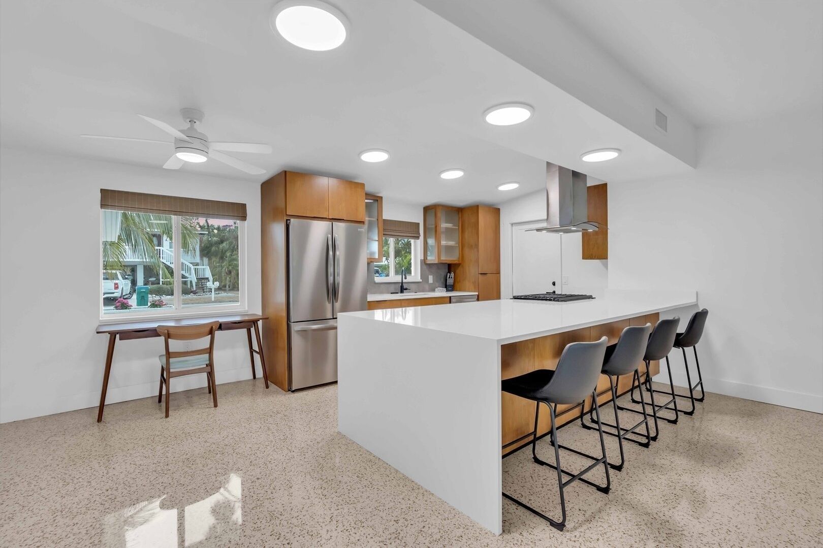 A modern kitchen with a central island, bar stools, and a refrigerator.