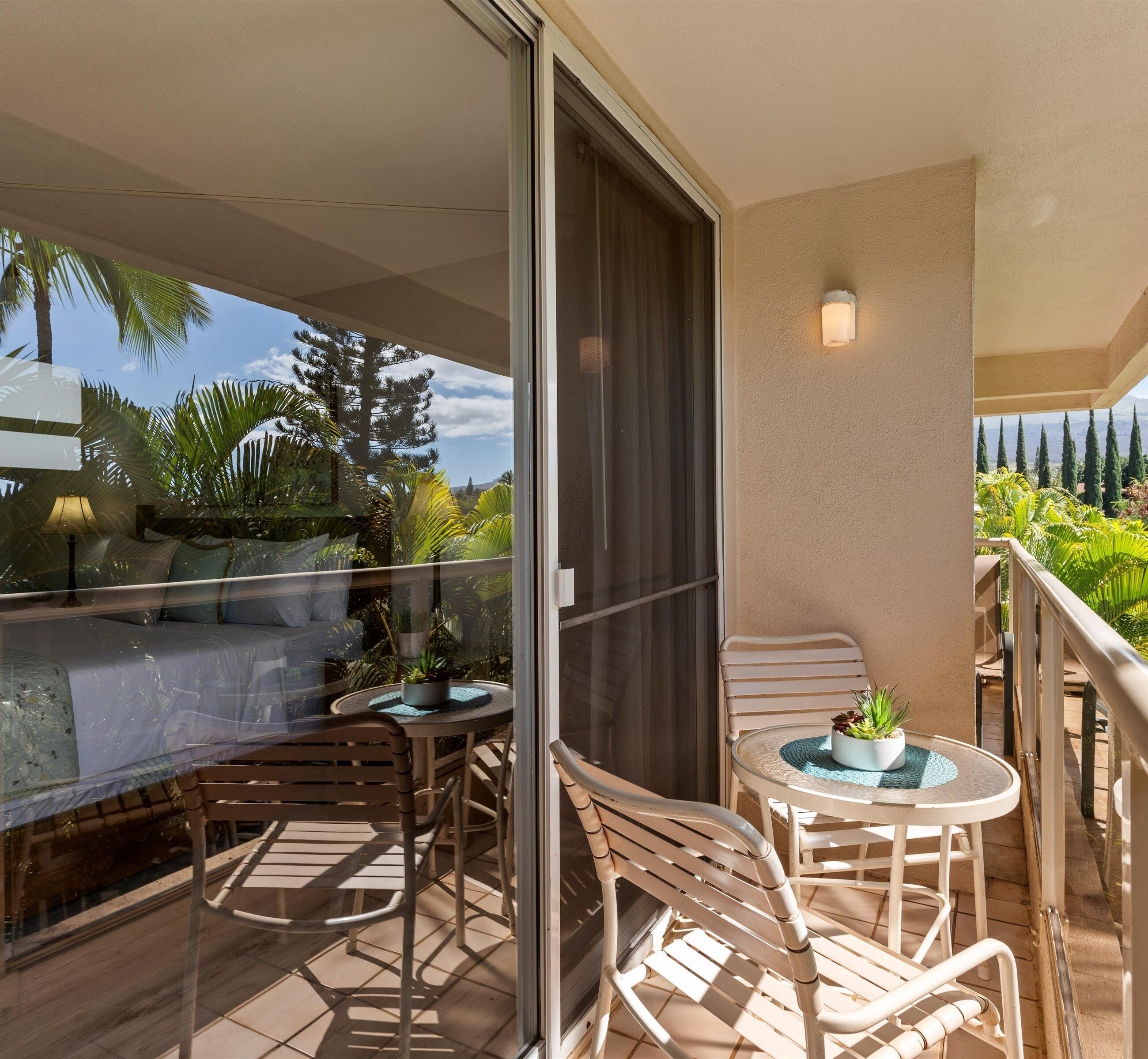 A balcony with a glass door, two round tables with chairs, a sofa, and a potted plant.