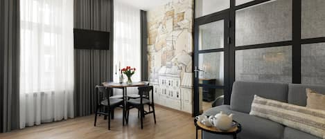 A modern living room with a grey sofa, a small round table with a teapot, and a wall mural of a cityscape.