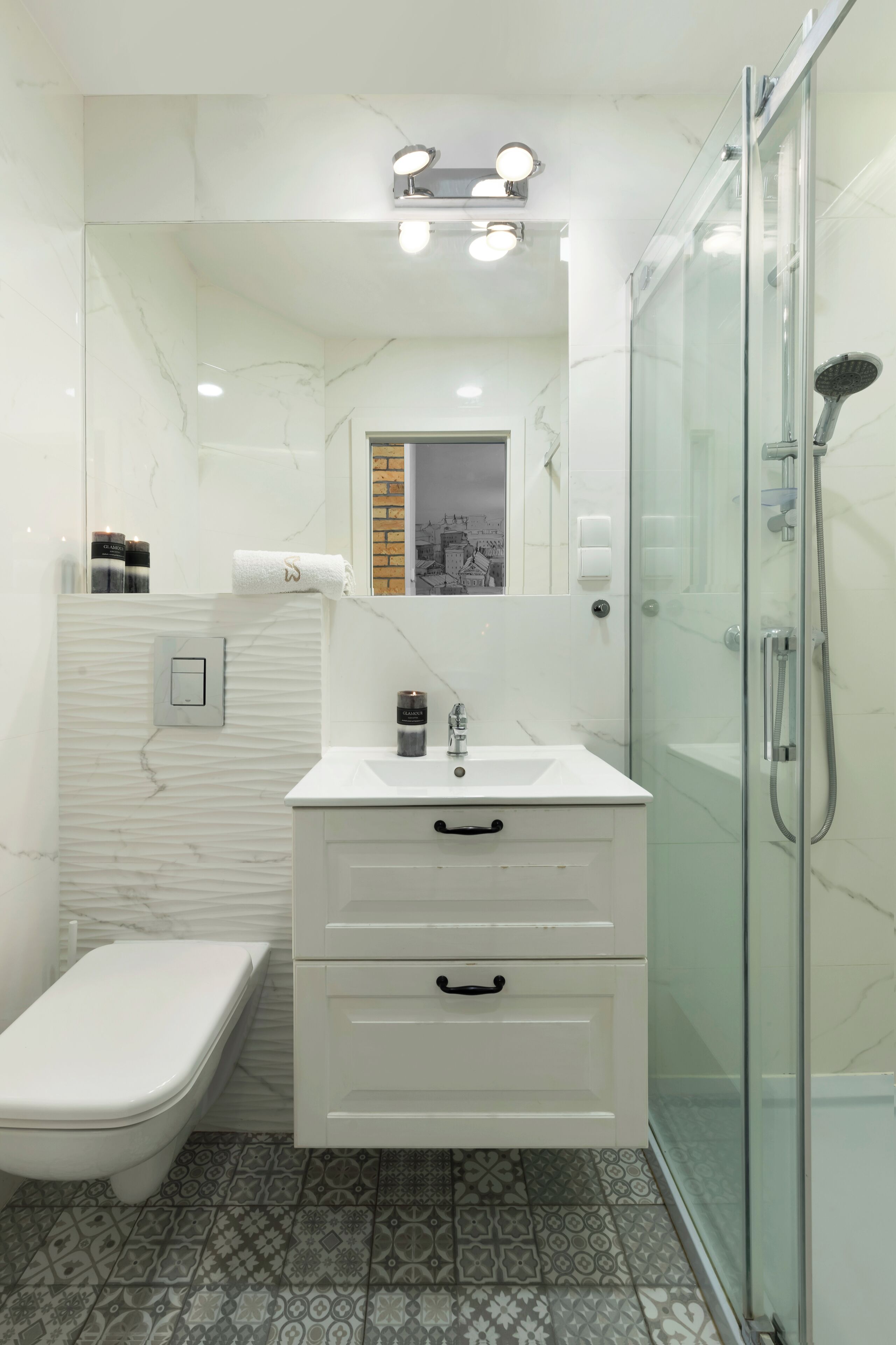 A modern bathroom with a white vanity, a glass shower enclosure, and patterned floor tiles.