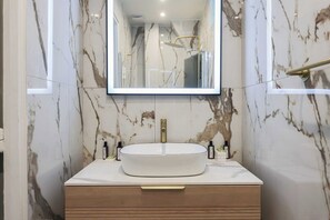 Un baño con tocador de mármol, un lavamanos redondo y un espejo grande.