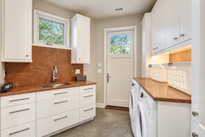 A compact kitchen with white cabinets, a marble countertop, a built-in washing machine, and a door with a window.