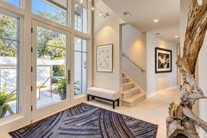 Un interior espacioso con una escalera, un banco y un ventanal grande con vista a un jardín.