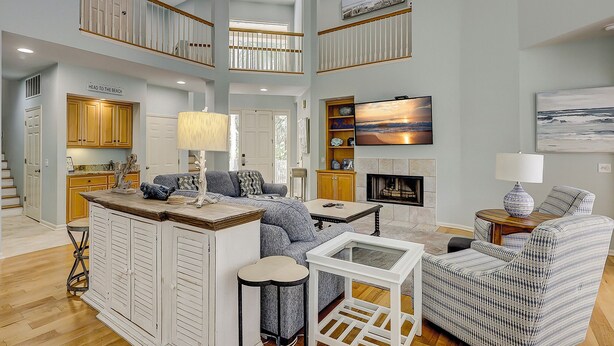 A spacious living room with a high ceiling, a fireplace, and a television mounted on the wall.