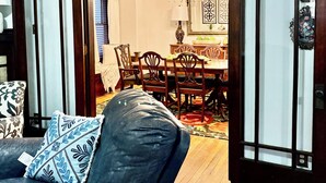 Una sala de estar con un sofá de cuero oscuro, un cojín estampado y una mesa de comedor de madera con sillas.