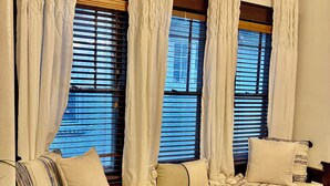 Una habitación acogedora con un banco de madera, cortinas blancas y vistas a través de persianas.