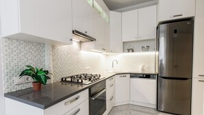 A modern kitchen with white cabinets, a stainless steel refrigerator, a gas stove, and a tiled backsplash. - Minsk Apartment Lux on Nezavisimosti 43 (Minsk)