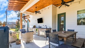 Un patio exterior con una parrilla, asientos y un televisor montado en la pared.
