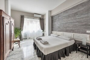 A bedroom with a large bed, a wooden wardrobe, a potted plant, and a window with curtains. - Regina Luxury Apartment in the Heart of San Giovanni (Roma)